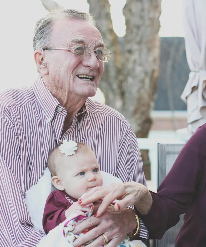 A smiling grandfather holding his baby granddaughter